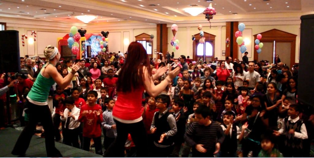 Dancing elves on stage in large room of kids